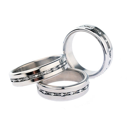 Two stainless steel cock rings with ball chain inlays, one ring showing the top view with the chain and the other showing the side view. The rings have a metallic finish and are adorned with small diamonds around the top edge.